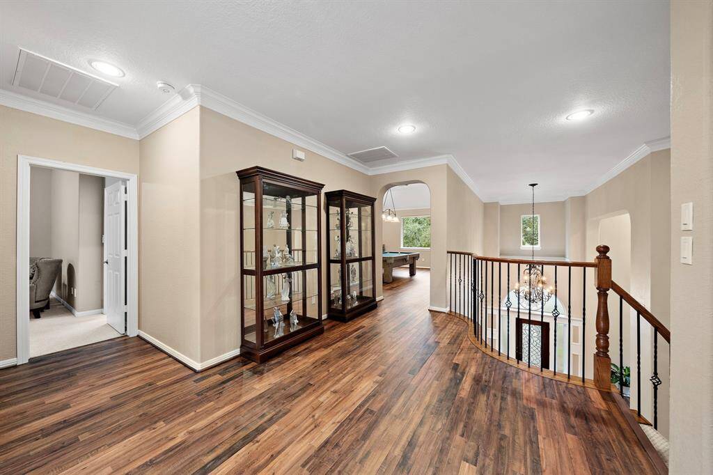 This spacious second-floor landing features elegant architectural details and flows to entertainment areas. Wood floors make the space inviting, while the wrought iron railing overlooks the elegant foyer below.