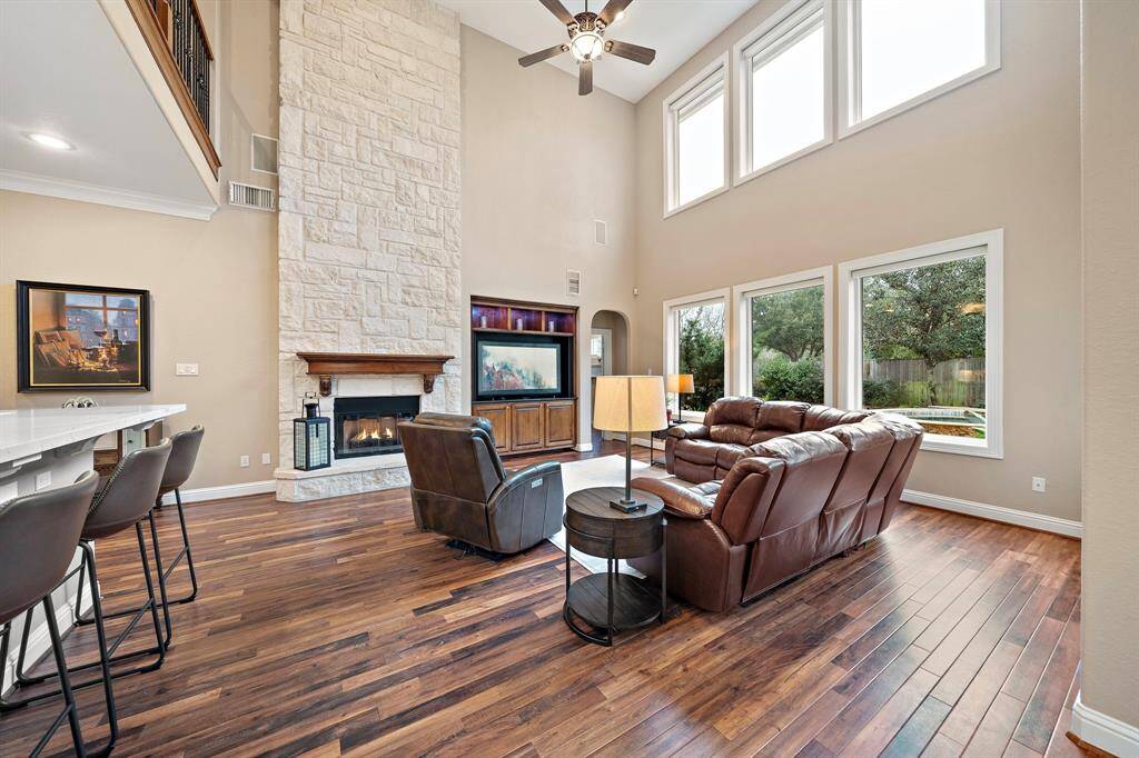 With soaring ceilings and expansive windows, the living area offers backyard oasis views and abundant natural light. The fireplace is framed by a stone accent wall, and the open layout flows into the kitchen. Enjoy updated flooring and a convenient seating bar.