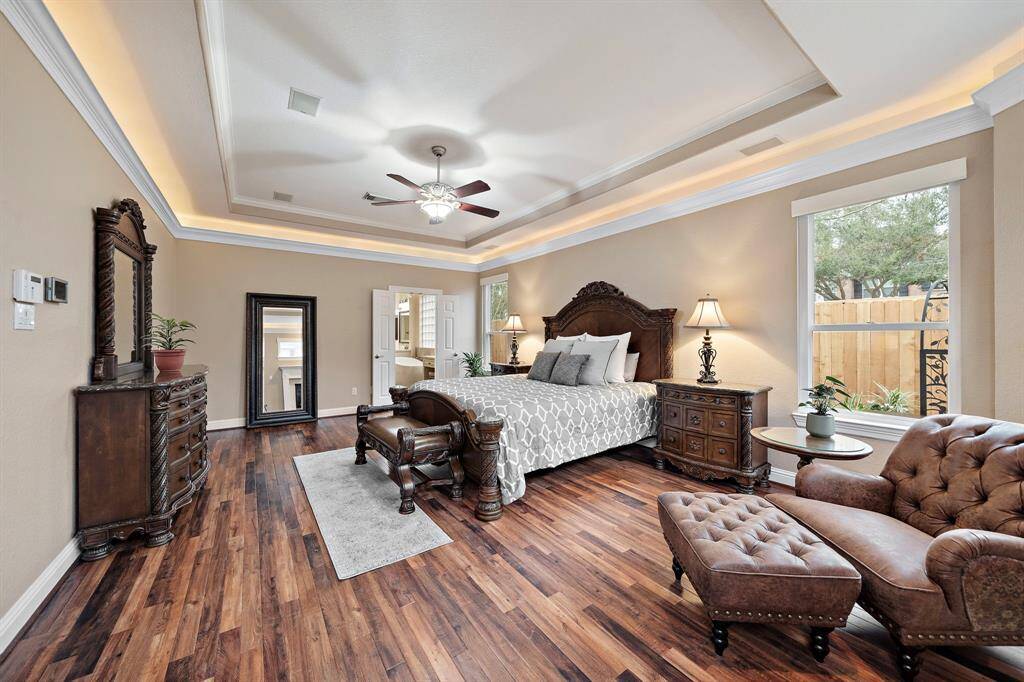 The primary bedroom is accentuated by detailed furnishings and wood floors. The tray ceiling is enhanced by accent lighting. Escape to the remodeled ensuite bath through the double doors.