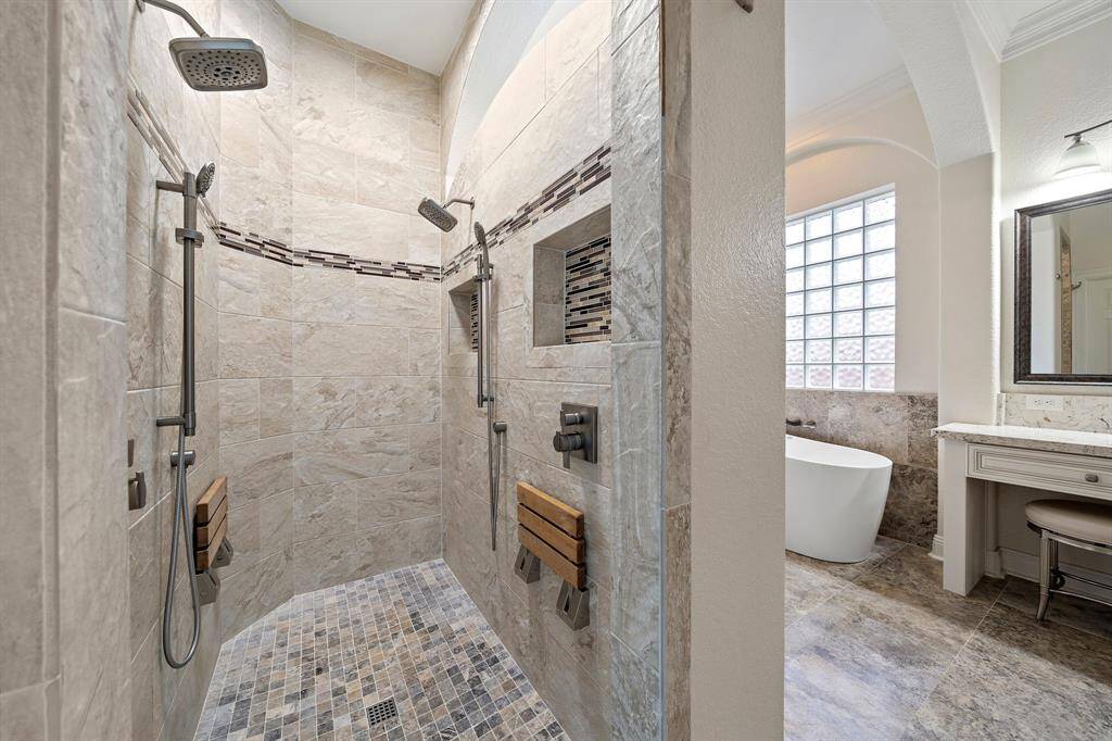 Walk into a spa-like primary bath featuring mosaic tile accents, dual shower heads, and seating in the walk-in shower. A soaking tub and vanity area enhance this luxurious ensuite. Updated fixtures complete the sleek space.