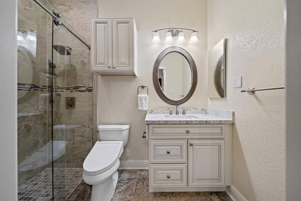 Elegant vanity offers storage space in this updated secondary bath. A framed oval mirror and sleek hardware adds luxury, while the tiled shower features glass doors and an adjustable shower head.