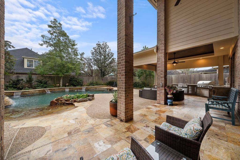 Covered patio delivers custom features, including a full outdoor kitchen and seating. A fire pit  creates refined outdoor living, while views extend out to the custom pool with waterfall features.