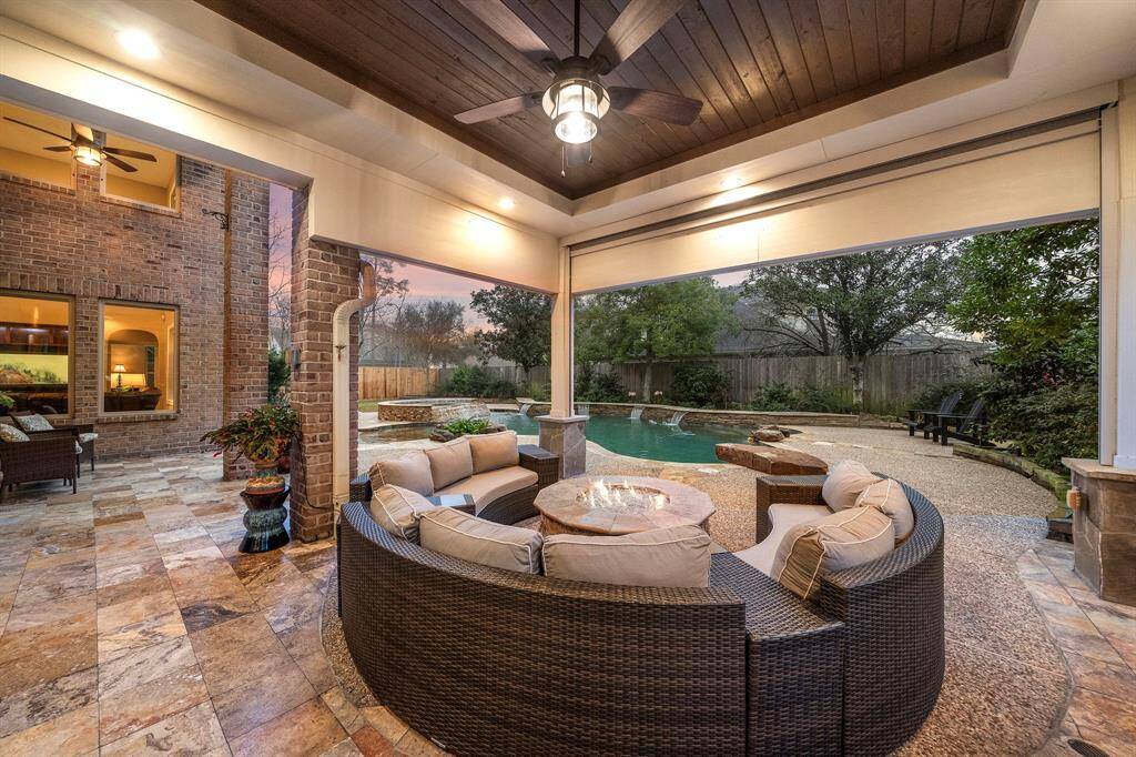 The covered patio offers a seamless blend of comfort and style with a rich wood-paneled ceiling, recessed lighting, and retractable shades. Overlooking the sparkling pool and lush landscaping, this outdoor retreat is perfect for relaxing evenings or entertaining in a resort-style setting.