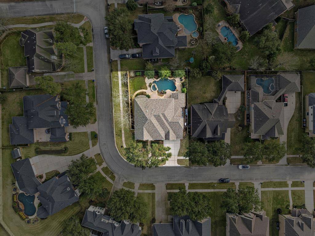 Aerial view showcases the Fall Creek home on its corner lot, complete with a heated pool and outdoor kitchen. Lush greenery surrounds the updated brick home, creating a private backyard retreat for resort-style living.
