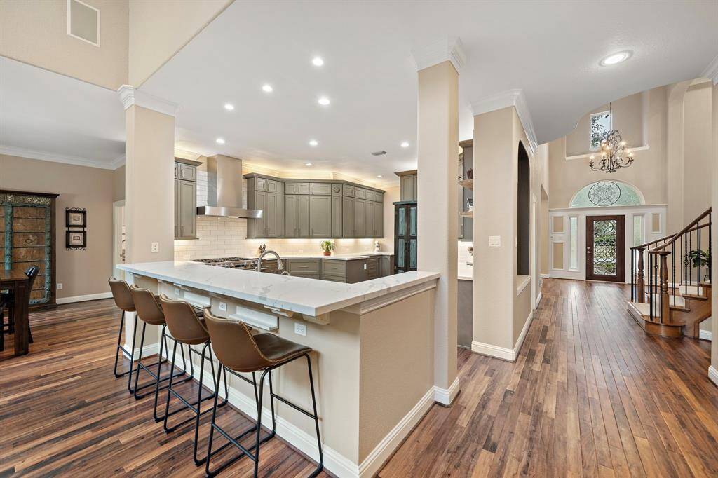 This open-concept layout offers an entertainer's vision from the kitchen, breakfast bar, and formal living area. Notice the sleek built-in vent hood, luxury appliances, elegant flooring and the entry with abundant natural light from newer, energy-efficient windows.