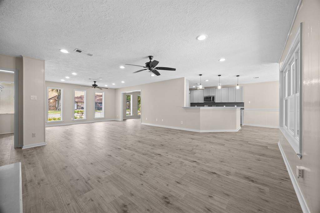 This is a spacious, open-plan living area with modern wood flooring, ample natural light from large windows, and contemporary kitchen with a breakfast bar.