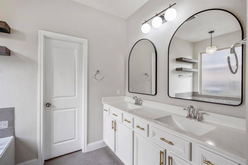 You'll love getting ready in this light and bright primary bathroom! The primary bathroom includes a large vanity with dual sinks, sleek white cabinets and countertops, modern framed mirrors, and brushed gold cabinet hardware.