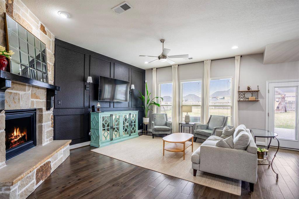 Step into elegance! This stunning living room boasts large windows, a custom accent wall, cozy fireplace, and rich wood floors, creating the perfect blend of warmth and sophistication.