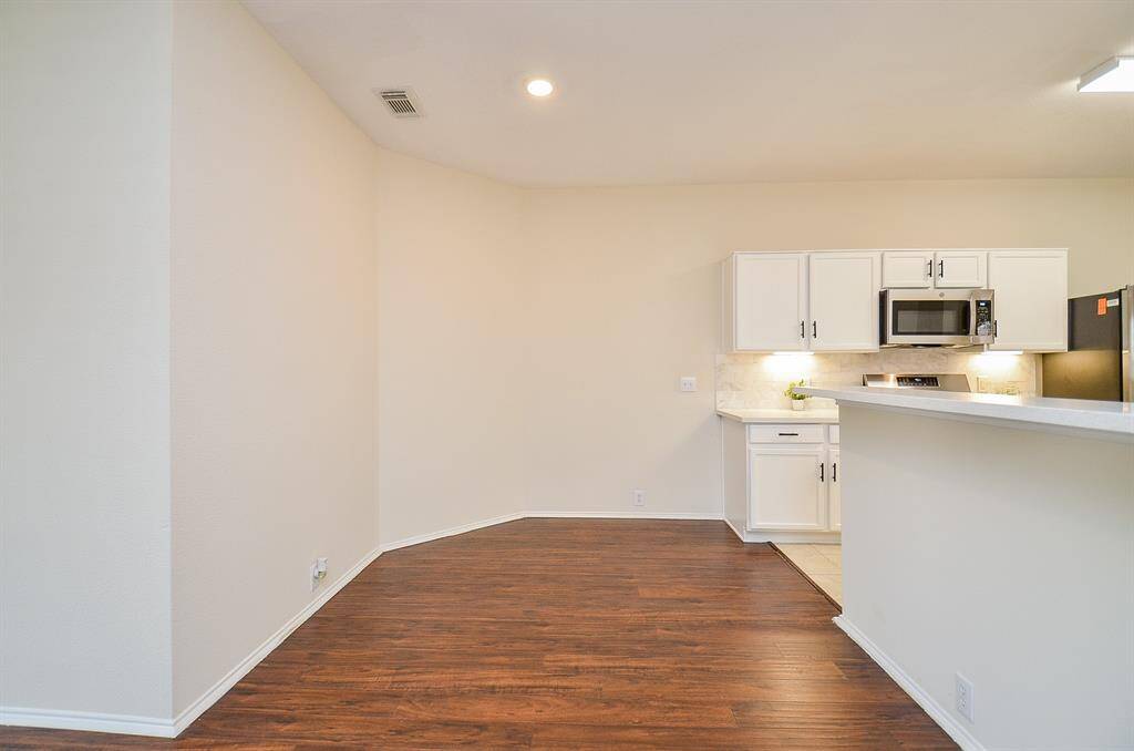 This photo showcases a bright, open kitchen and dining area with hardwood floors. The kitchen features white cabinets, a modern microwave, and sleek countertops, offering a clean and inviting space for cooking and dining.