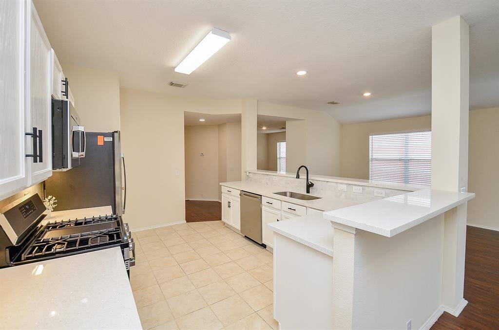 Bright, modern kitchen with light countertops and cabinetry, stainless steel appliances, and tile flooring. Open layout with a breakfast bar and ample natural light from large windows.