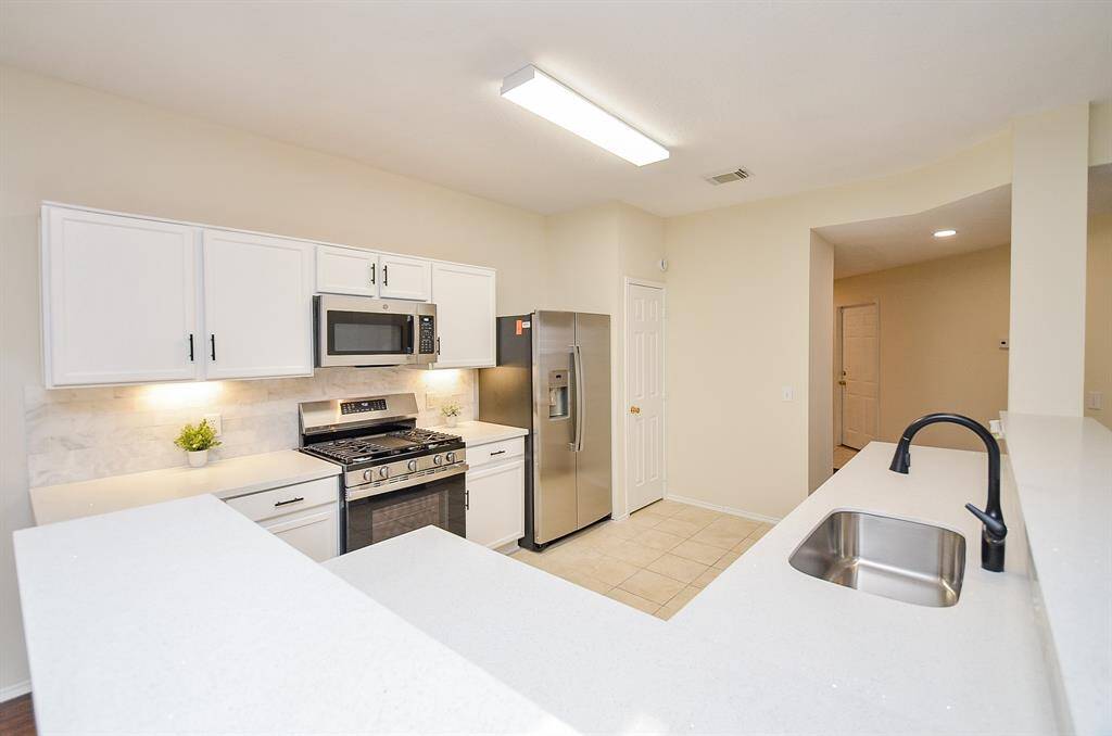 Bright and modern kitchen with white cabinets, stainless steel appliances, and a central island with a sink. The open layout and neutral tones create an inviting space.
