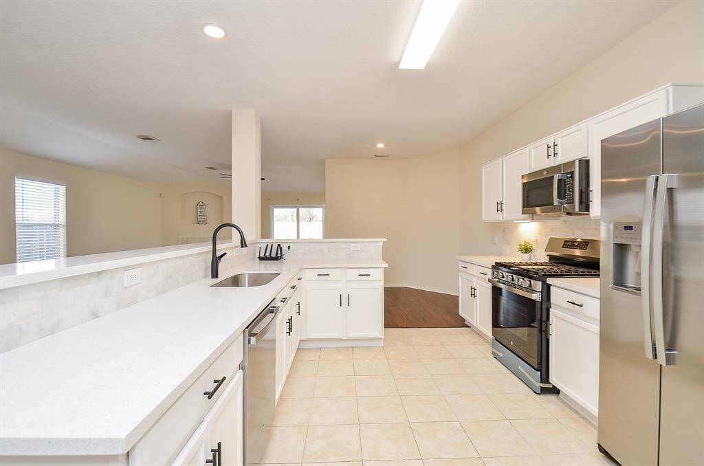 This kitchen features modern stainless steel appliances, white cabinetry, and a spacious layout with a breakfast bar. The open concept design flows into a bright living area, creating a welcoming space for entertaining.