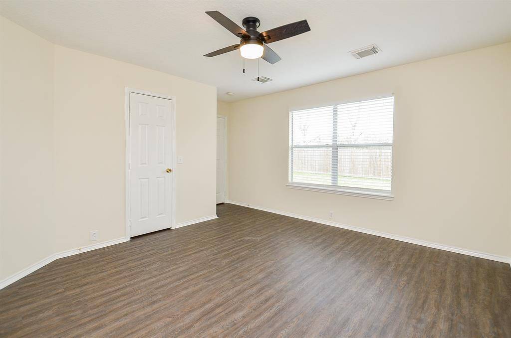 This room features neutral walls, wood-style flooring, a large window offering natural light, and a ceiling fan for comfort. Perfect for a bedroom or home office.