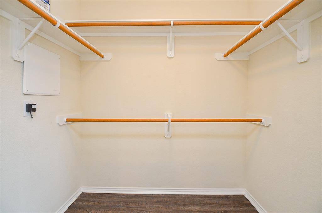 Spacious walk-in closet with multiple wooden rods for ample hanging space, clean beige walls, and a dark wood floor. Ideal for organized storage.