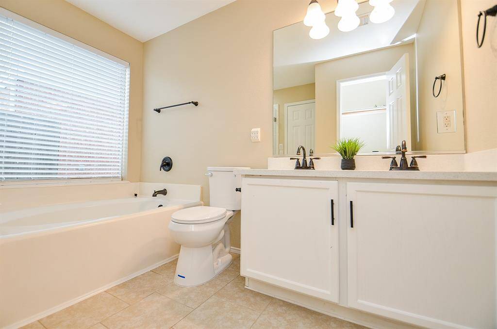 Bright and spacious bathroom featuring a large bathtub, dual sinks with modern fixtures, a sizable mirror, and ample natural light from a window with blinds.