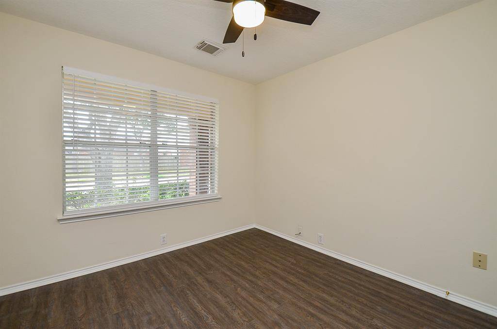 This room features neutral walls, wood-look flooring, a large window with blinds, and a ceiling fan with a light, offering a bright and airy space.