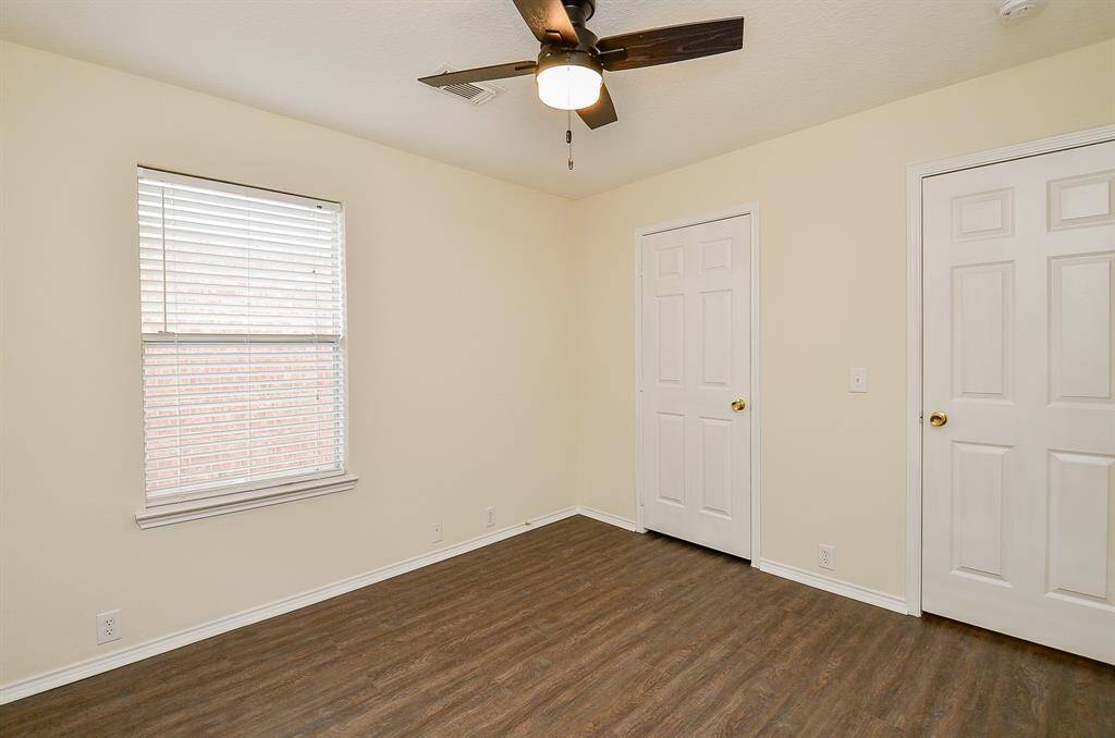 This room features neutral walls, hardwood flooring, a ceiling fan, and ample natural light from a large window. Ideal for a bedroom or office space.