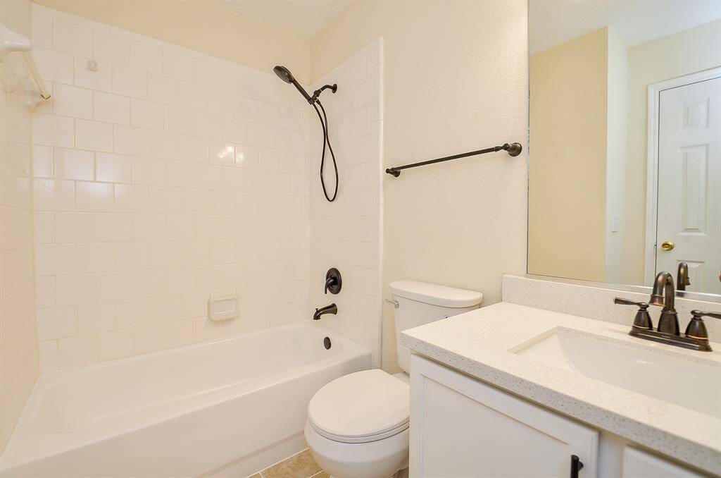 This bathroom features a clean, modern design with a white tiled shower-tub combo, sleek black fixtures, a white vanity with a quartz countertop, and ample lighting.