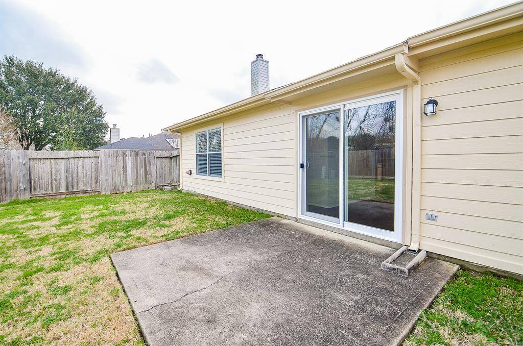 This photo shows a cozy backyard with a small concrete patio area, fenced for privacy. It features a sliding glass door leading into the house, perfect for easy indoor-outdoor access.