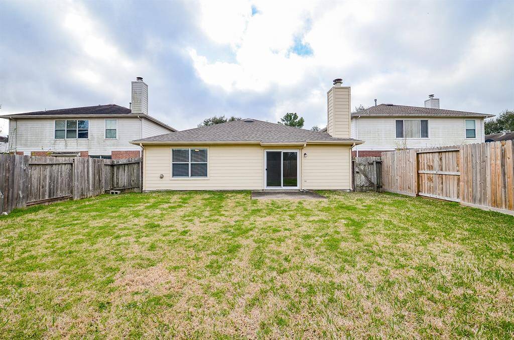 This photo shows the backyard of a single-story home with a fenced lawn and a back patio area. The house has light siding and a chimney, offering a private outdoor space ideal for families or entertaining.