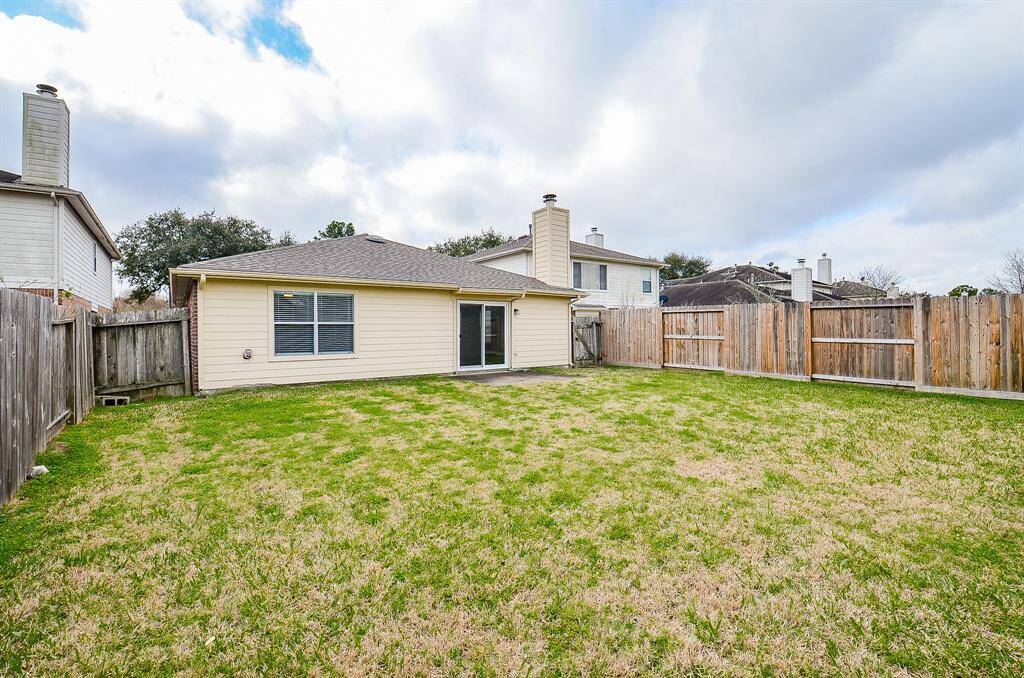 Spacious backyard with a well-maintained lawn, wooden fencing, and a single-story house featuring a chimney and sliding glass doors. Perfect for outdoor activities and privacy.