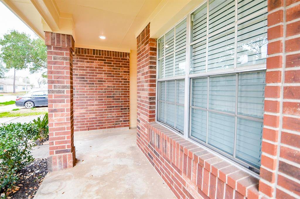 This inviting home features a cozy front porch with charming brickwork and large windows, perfect for relaxing and enjoying the neighborhood view.