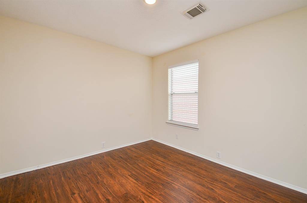 This room features hardwood floors, neutral-colored walls, and a window providing natural light. It's a simple, versatile space suitable for a bedroom or office.