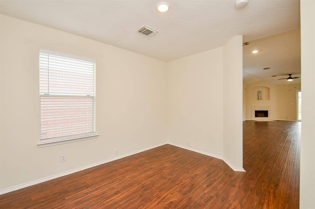 This photo shows a bright, open living space with wood flooring, neutral walls, and recessed lighting. It features a window with blinds and a view into a room with a fireplace, providing a welcoming and versatile area for living and entertaining.
