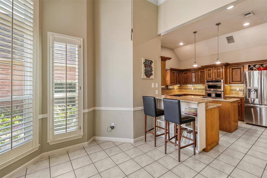 Another view of large island kitchen from breakfast area showing breakfast bar with built-in bookcase, pendent and recessed lighting, stainless appliances, and tile flooring.