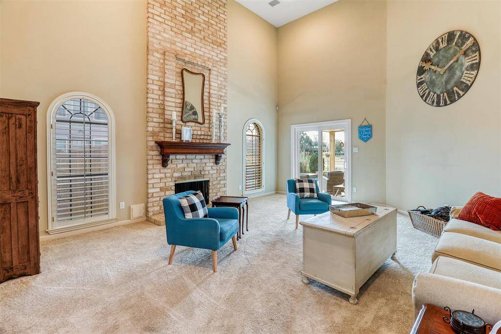 Another view of soaring 2-story family room showing floor to ceiling brick gas log fireplace, large windows with shutters offering lots of natural light, and recently upgraded sliding back door into backyard covered patio and pool area.