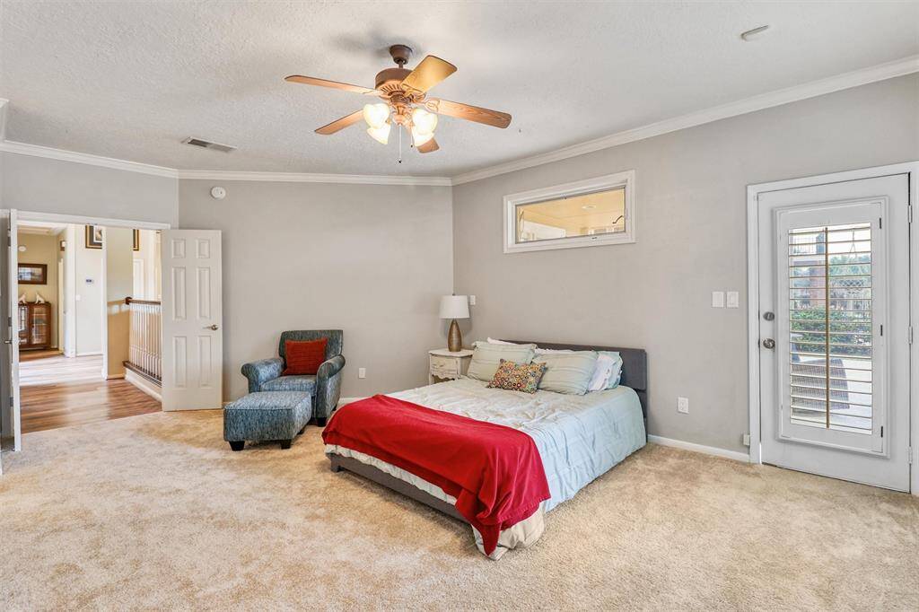 Another view of large primary bedroom featuring crown molding, ceiling fan, recent carpet, shuttered private door leading to backyard covered patio and pool.