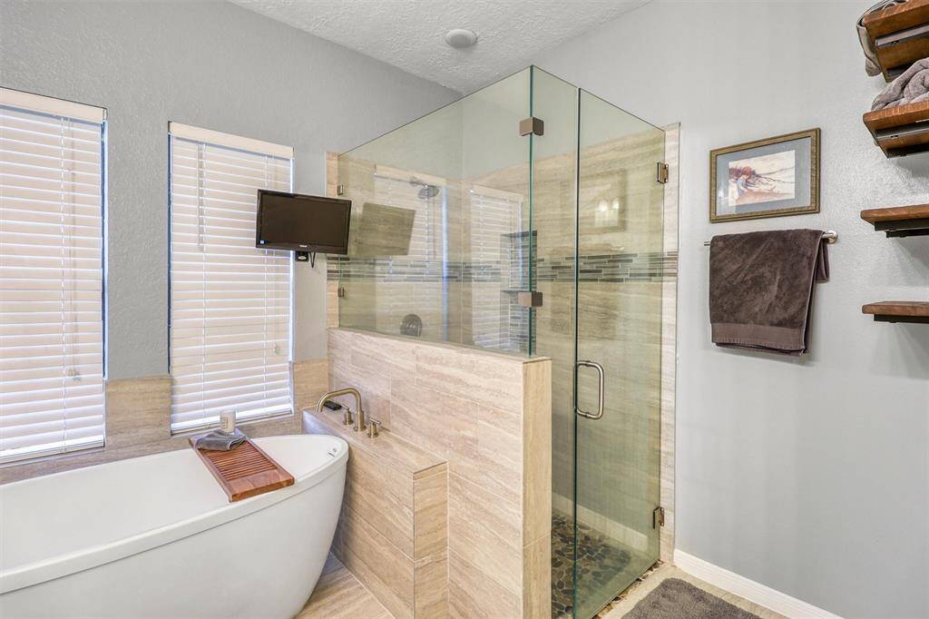 Remodeled oversized walk-in shower with glass enclosure, large spa-like soaker tub, and TV which conveys with properety.