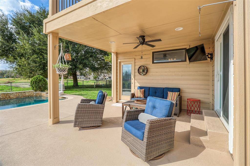 Beautiful view of outside covered back patio featuring ceiling fan and wall mounted TV that conveys with property.