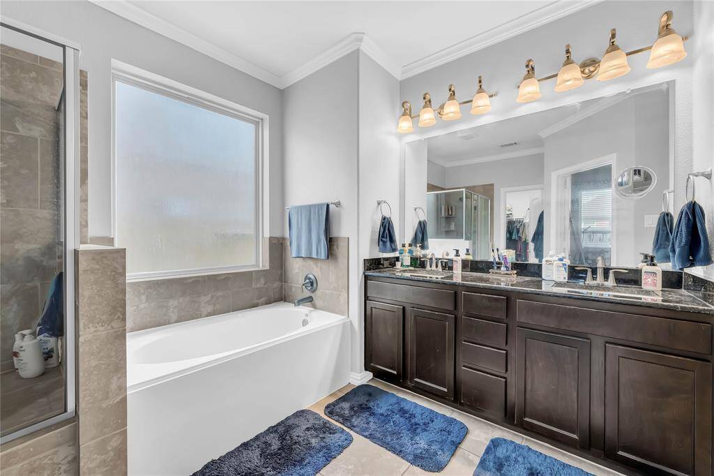 This bathroom features a modern design with a spacious bathtub, a separate glass-enclosed shower, and a dual-sink vanity with dark wood cabinets. It offers ample lighting and a sleek, tiled floor for a polished look.