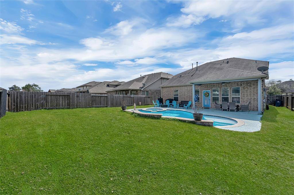 Spacious backyard featuring a well-maintained lawn, a swimming pool with surrounding patio area, and a brick house with a covered patio. It offers a private, fenced space perfect for outdoor relaxation and entertainment.