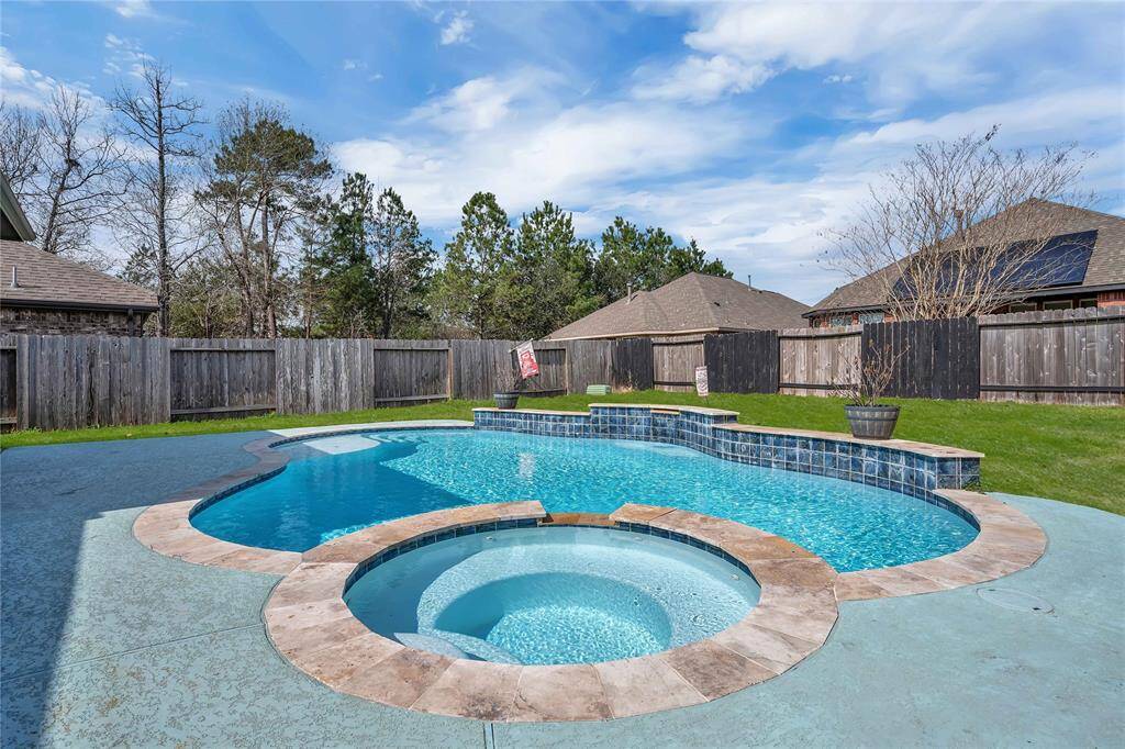 A spacious backyard features a beautiful pool with a spa, surrounded by a wooden fence for privacy. The area offers ample space for relaxation and entertainment, with some landscaping elements and a clear view of the sky.