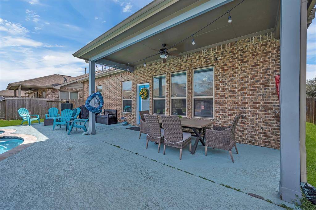 This backyard features a spacious patio with a covered area, perfect for outdoor dining with a table and chairs. It includes a cozy seating area with vibrant blue chairs by a pool, creating an inviting space for relaxation and entertaining. The brick exterior adds a warm touch.