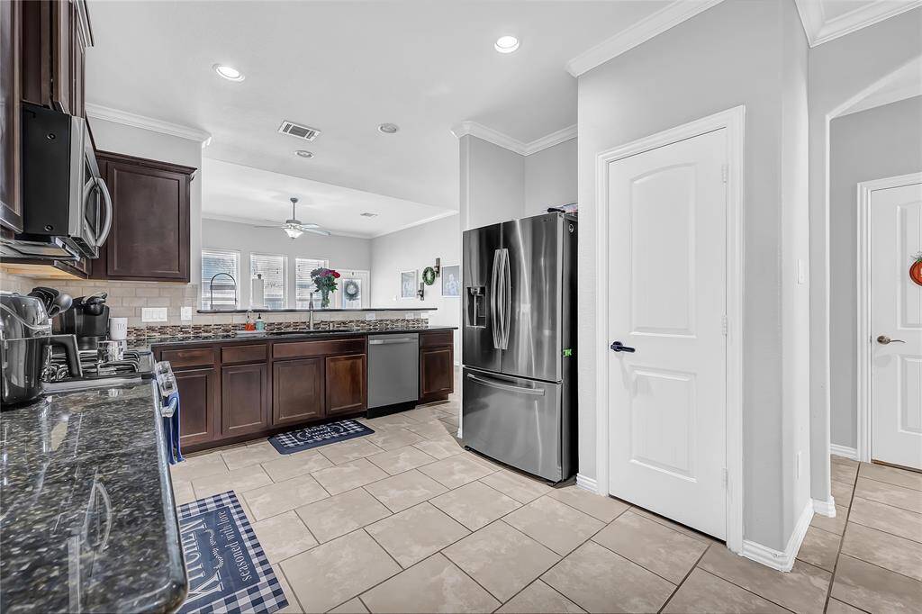 This modern kitchen features stainless steel appliances, dark wood cabinetry, and granite countertops. The space is brightened by recessed lighting and a window, with a tiled floor and neutral walls creating a clean, inviting atmosphere.