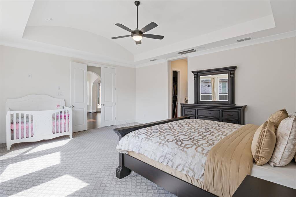 Spacious primary bedroom featuring elegant tray ceilings, abundant natural light, and a stylish ceiling fan for added comfort.