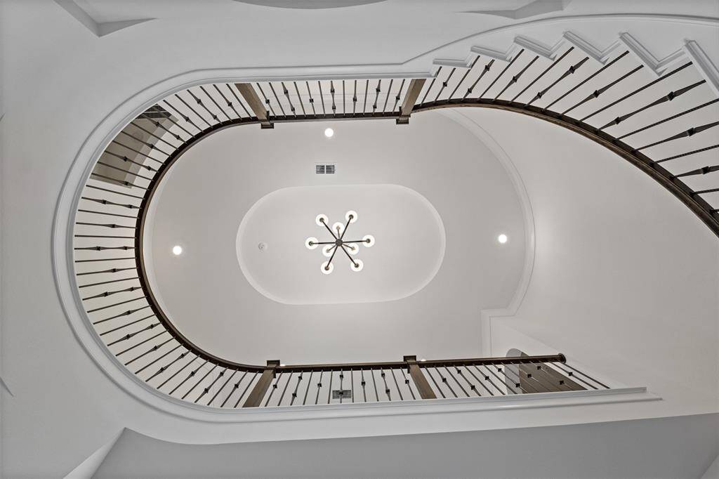 Elegant curved staircase, viewed from below. The ceiling features a modern chandelier, creating a sophisticated focal point.