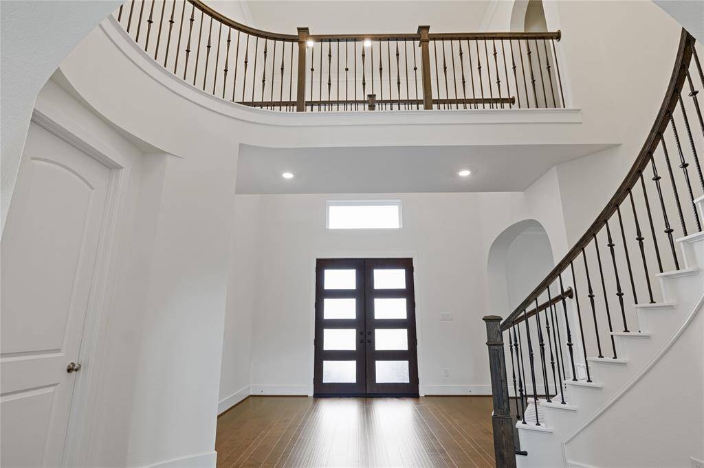 Spacious entryway with high ceilings, a sleek dark wooden front door, and a curved staircase featuring elegant iron balusters. The area is filled with natural light, creating an inviting atmosphere.