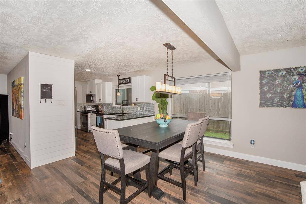 This photo showcases a modern kitchen with sleek black countertops, white cabinetry, and stainless steel appliances. The space features a stylish backsplash, wood flooring, and ample natural light, leading into a cozy dining area.