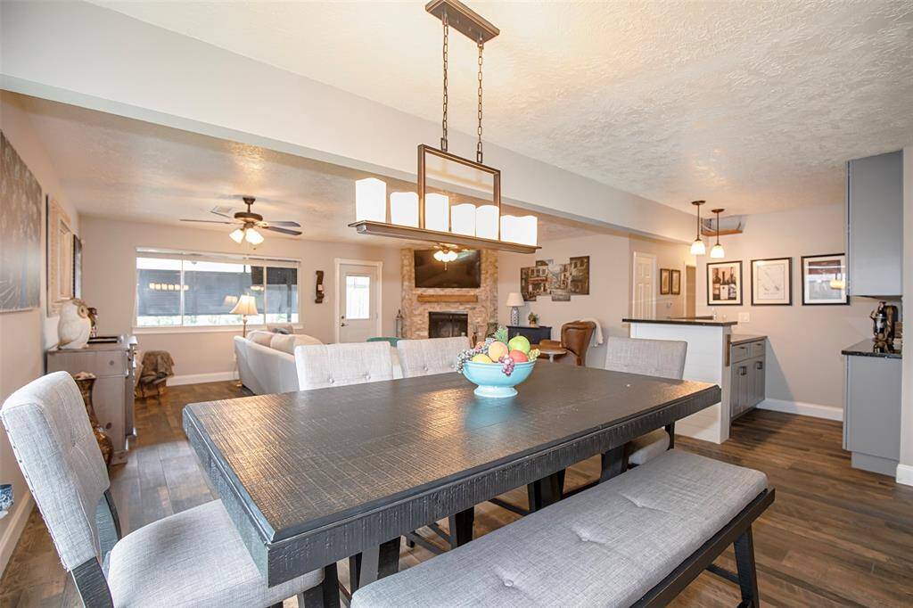 This photo features a cozy living space with a modern bar area. The bar has sleek black countertops and tasteful cabinetry, complemented by stylish pendant lights. The adjoining living room has a warm, rustic feel with a stone fireplace and wood accents.
