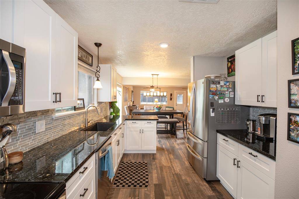 This inviting open-concept space features a cozy dining area with a modern light fixture, a spacious living room with a stone fireplace, and a well-equipped kitchen with a breakfast bar. The room is bright, with large windows and warm wood flooring, creating a welcoming atmosphere for entertaining and family gatherings.