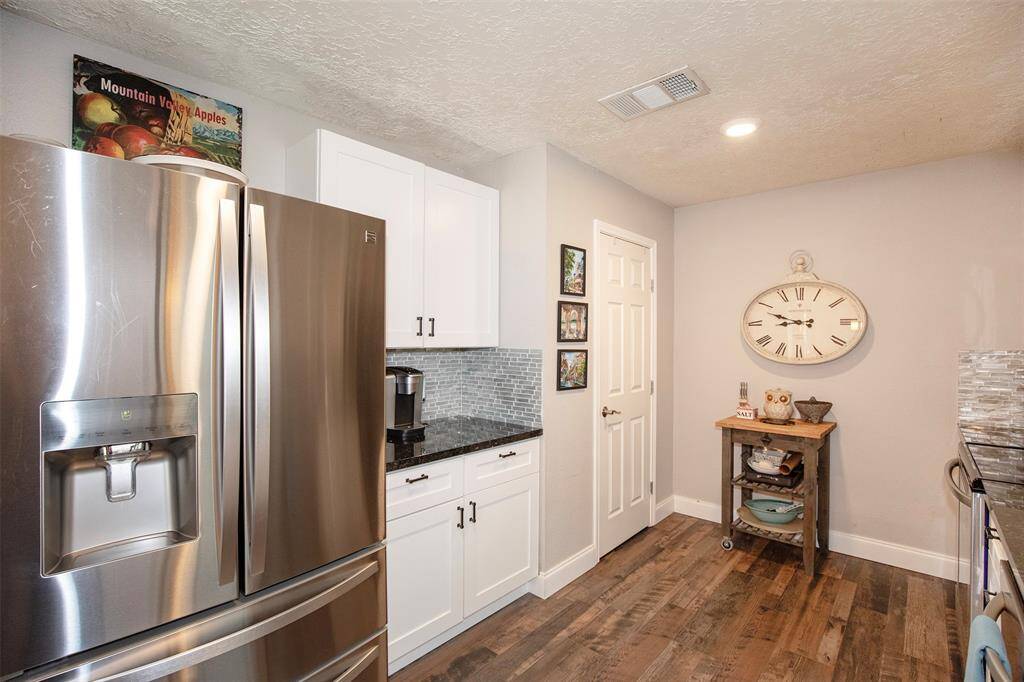 This open-concept living area features a large space with many furniture placement options and a stone fireplace. The space extends into a dining area and modern kitchen with a breakfast bar. Ceiling fans and wood flooring add warmth and style to the room.