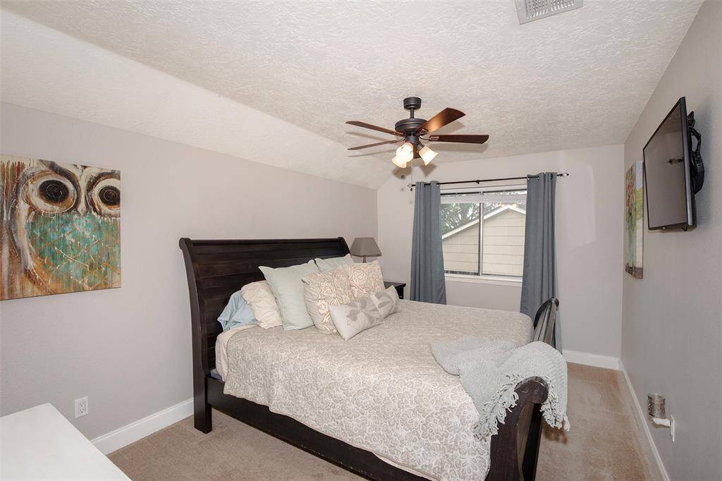 This room is a cozy home office with neutral walls, carpeted flooring, and a ceiling fan.