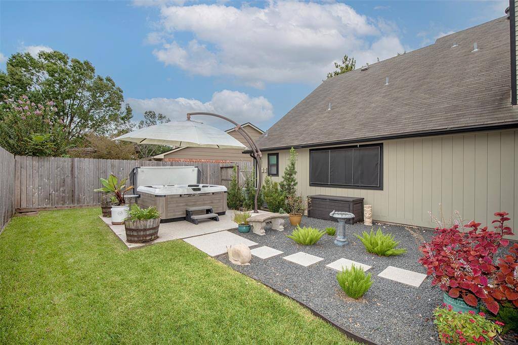 This photo showcases a spacious covered patio with ceiling fans, comfortable seating, built in barbecue grill and beverage fridge. It offers a view of a cozy backyard, ideal for entertaining and relaxation.