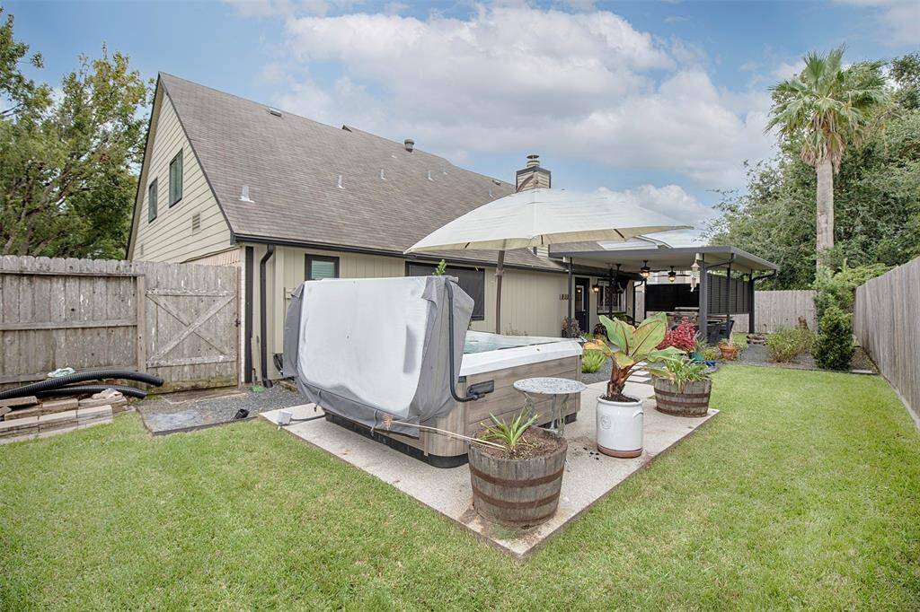 This outdoor space features a covered patio with ceiling fans, comfortable seating area, and a built-in grill. The area opens to a landscaped backyard with a stone path leading to your outdoor spa.