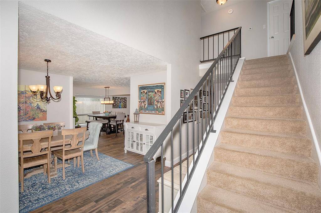 This photo showcases a welcoming entryway with carpeted stairs leading to the upper level, and a view into a cozy dining area with hardwood floors and elegant lighting. The space features tasteful decor and a warm, inviting atmosphere.