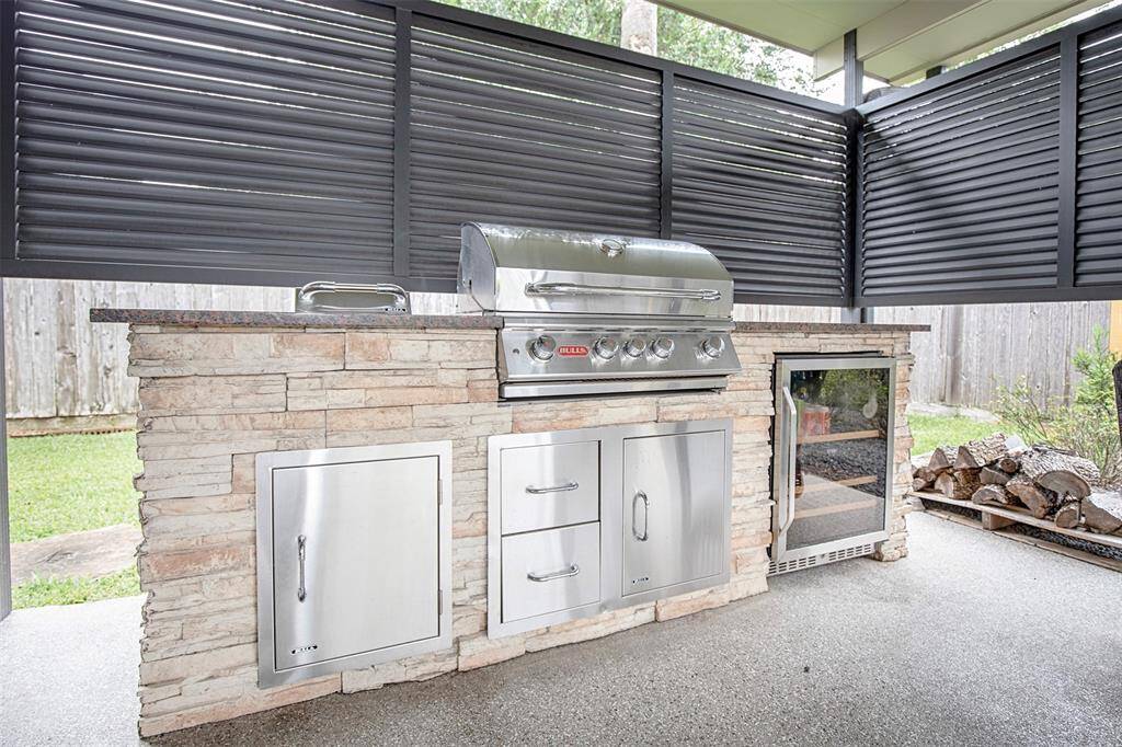 This outdoor space features a covered patio with ceiling fans, comfortable seating, and a built-in grill area. Surrounded by lush greenery it's the perfect space for relaxing or entertaining.